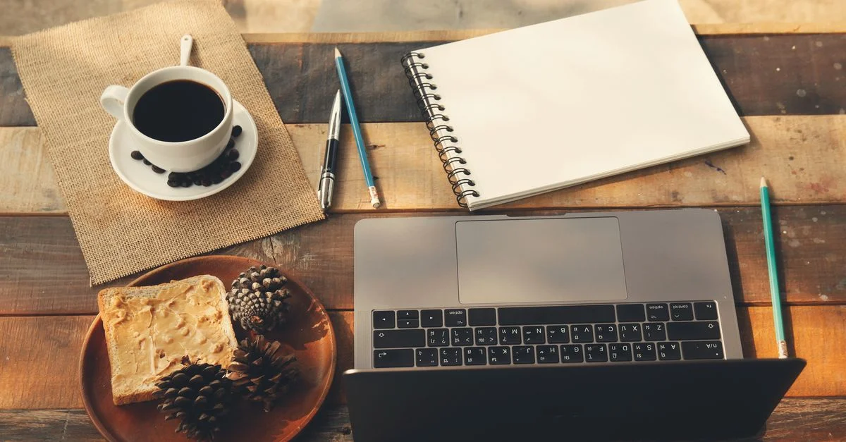 Un espace de travail à domicile chaleureux et accueillant avec une tasse de café, un ordinateur portable et un bloc-notes sur une table en bois.