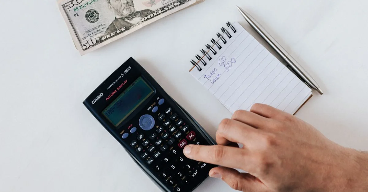 Une main utilisant une calculatrice à côté d'un bloc-notes et de l'argent, représentant la planification financière.